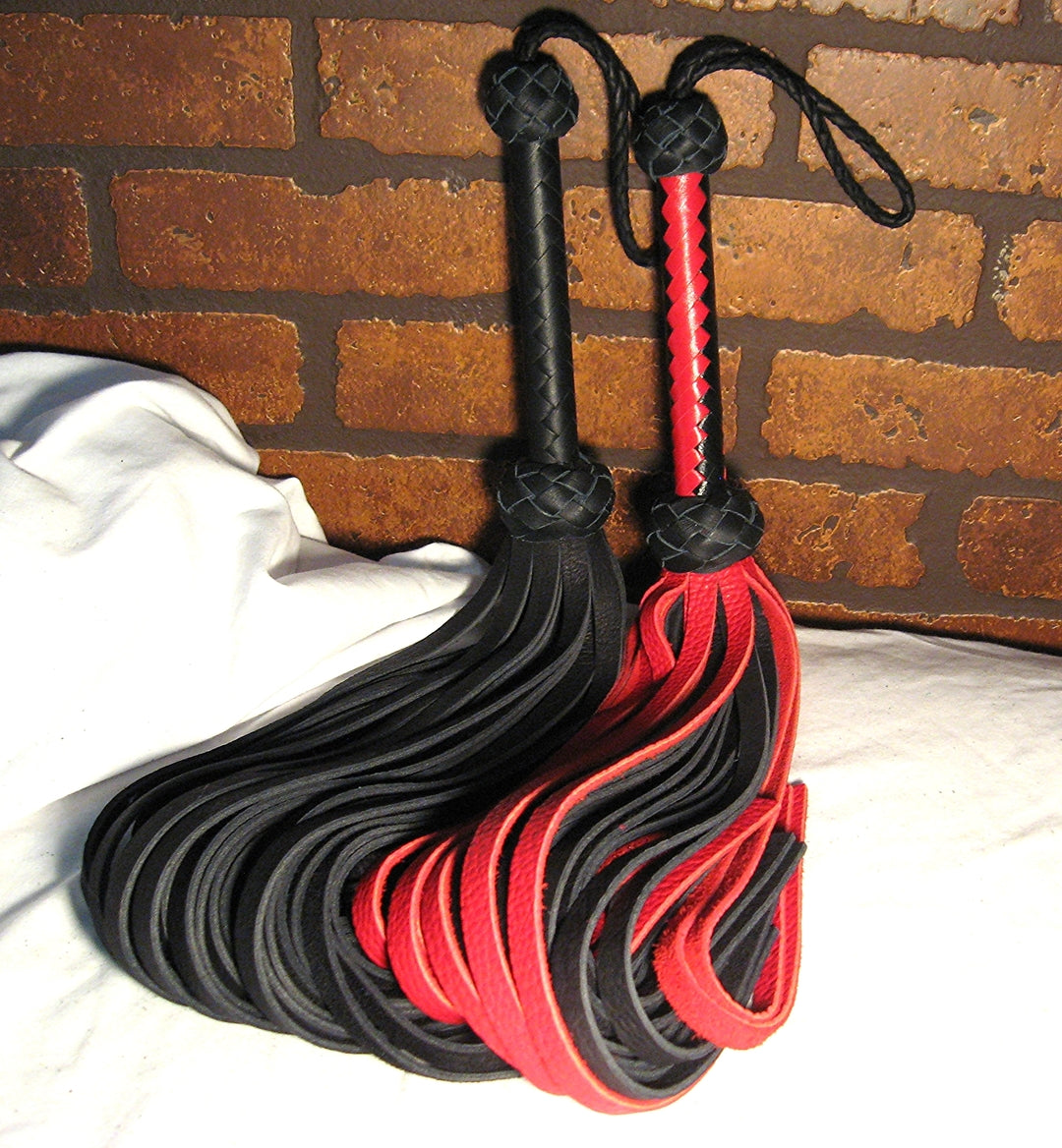 A black buffalo flogger and a red buffalo flogger sitting up side by side against a brick wall background.