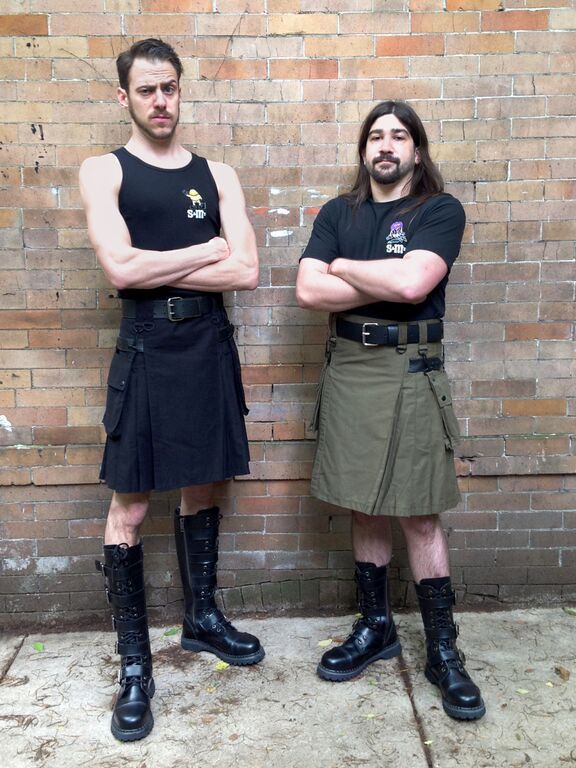 Two models, one wearing a black and the other wearing a green heritage kilt.