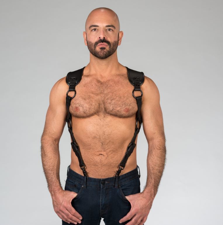 A shirtless masculine model wears the Carpenter Suspender Harness with the front metal clips attached to the belt loops of his jeans.