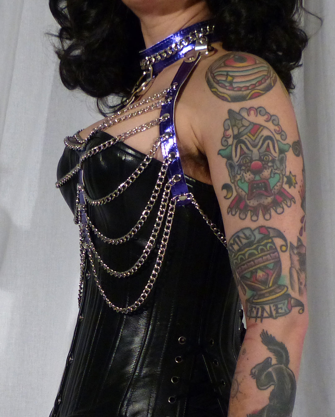 A side view of a model wearing the purple leather and chain three column halter harness over a black bust corset.