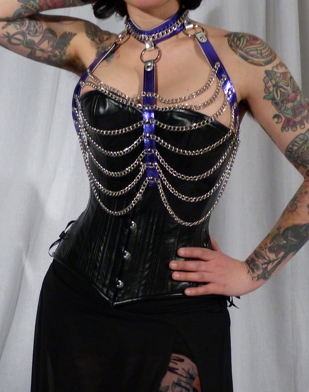 A model wearing the purple leather and chain three column halter harness over a black bust corset.