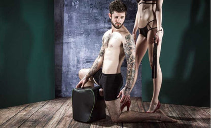 Two models posing, on standing, holding a whip, the other kneeling over the Fleshlight Top Dog Mount with a fleshlight in it.