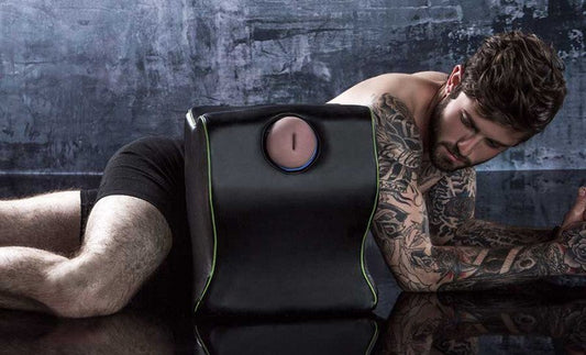 A tattooed model posing behind the Fleshlight Top Dog Mount with a fleshlight inside it.