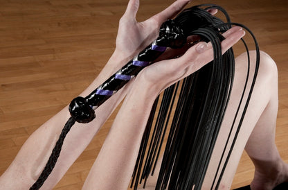 Two hands offering a Revenge Flogger with purple and black handle.
