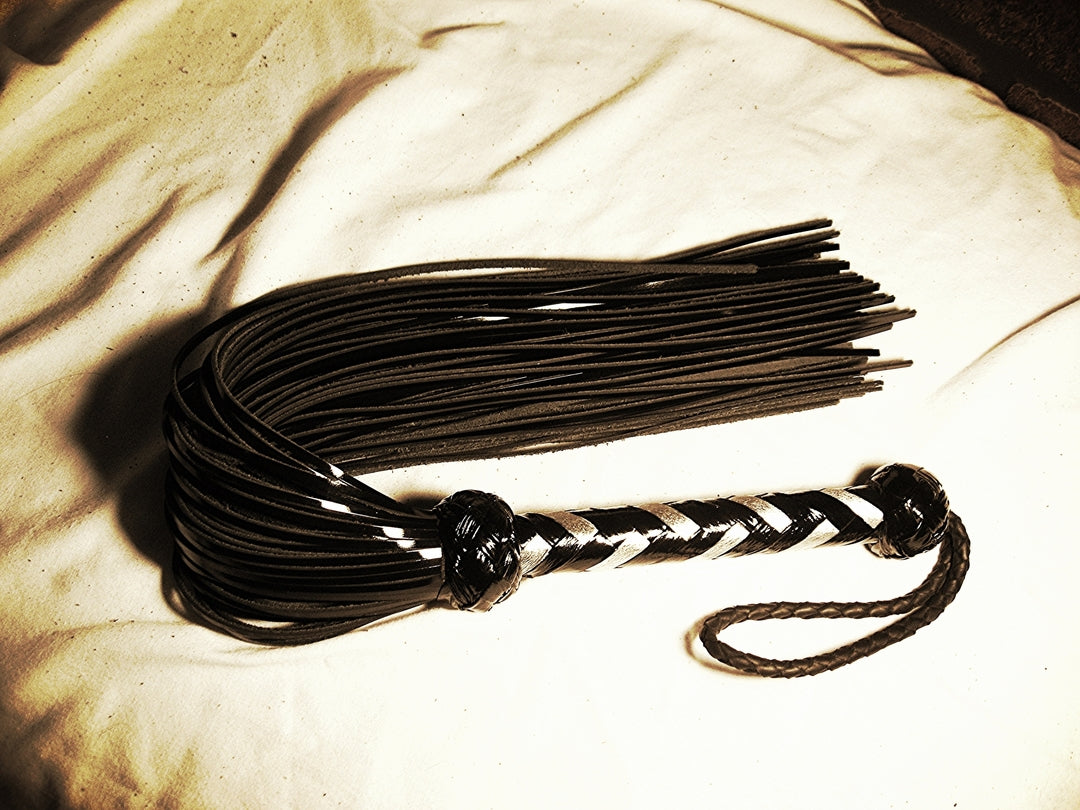 Black Revenge Flogger with silver and black handle, curled up.