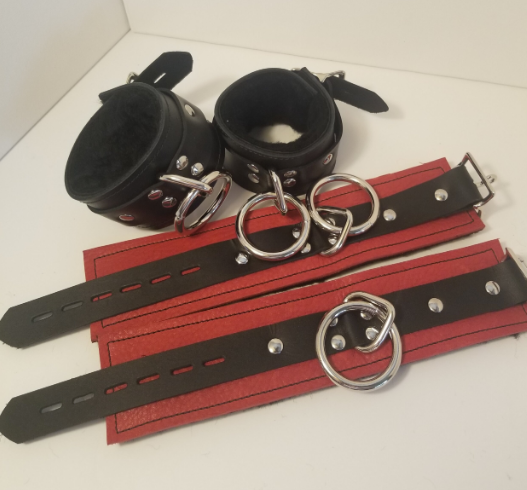 Another camera angle of a pair of black Basic Fleece Wrist Restraint Cuffs displayed buckled, and a red pair displayed laying flat.