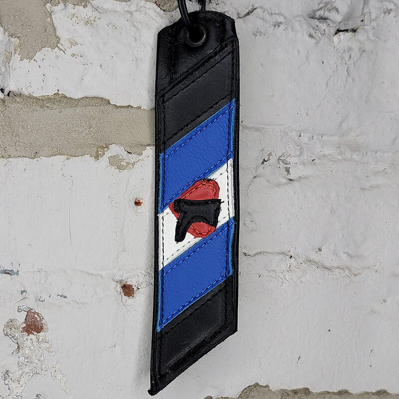 Boot Black Pride flag key ring against a wall