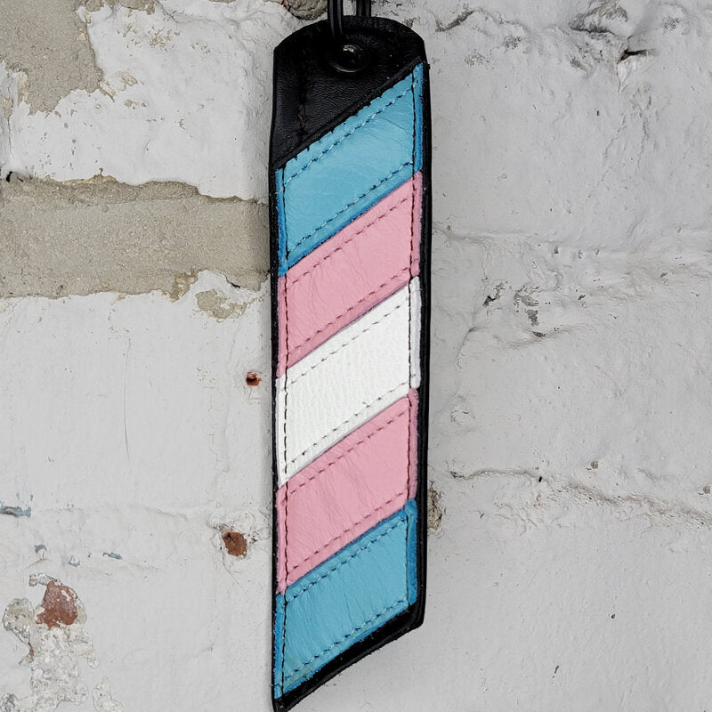 Transgender pride flag key ring against a wall
