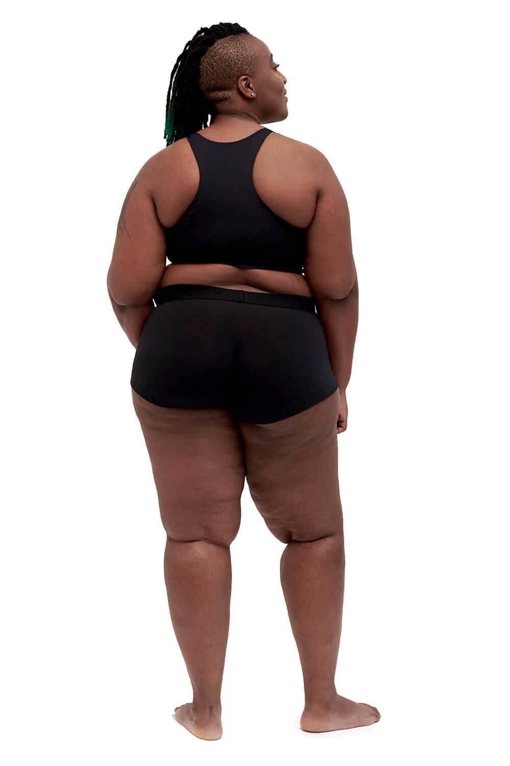 A model in black spandex shorts shows the rear view of the black Gentle Binding Compression Top.