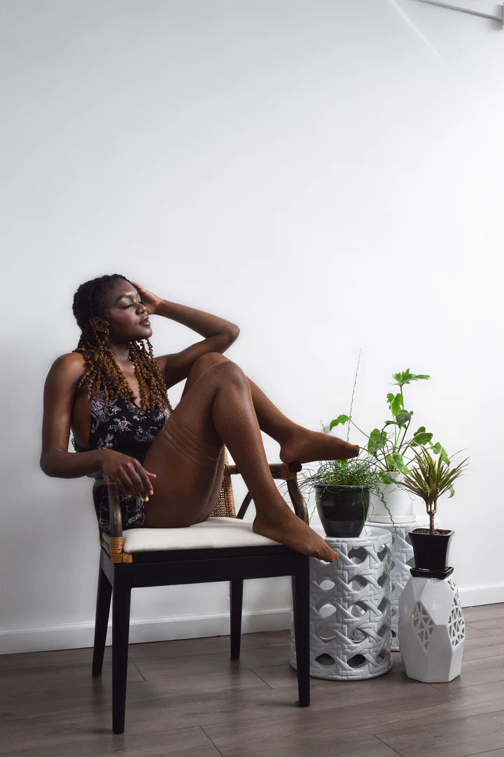 model sitting in chair with leg on the arm of the chair wearing the Andie Chocolate Fishnet Thigh Highs