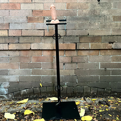 The Ballistic Cock and Ball Pillory with a dildo being squeezed between the plates.