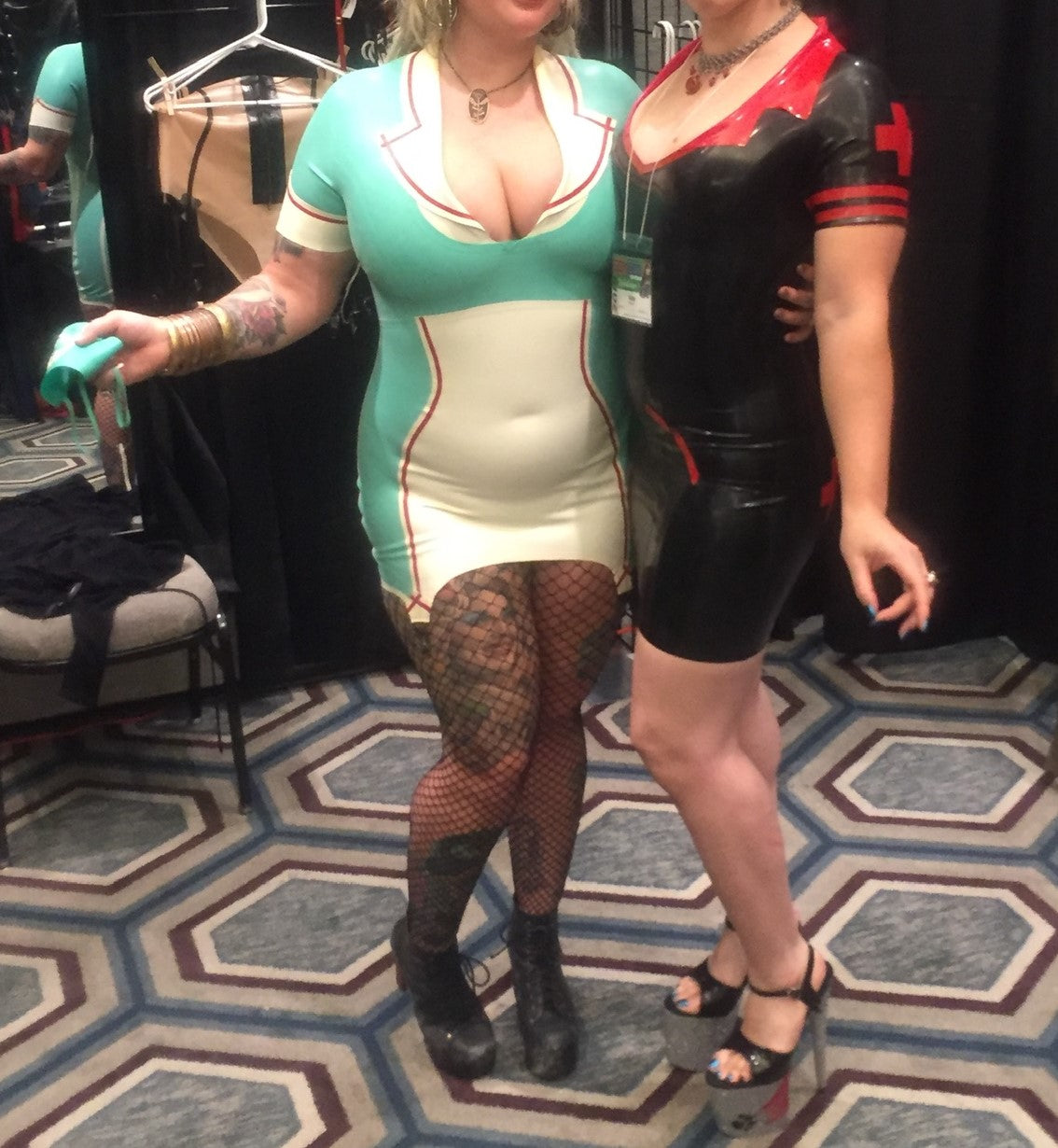 Two models wearing latex nurse costumes. One is black and red and the other is the Latex Natasha Nurse Dress & Cap. 
