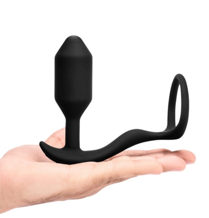 A hand holds out the black toy, which consists of a torpedo-shaped insertable weighted bulb, a thin neck, a flexible T-shaped base, a long arm stretching off the front of the base, and a ring at the end of the arm. It's made out of sleek matte black silicone.