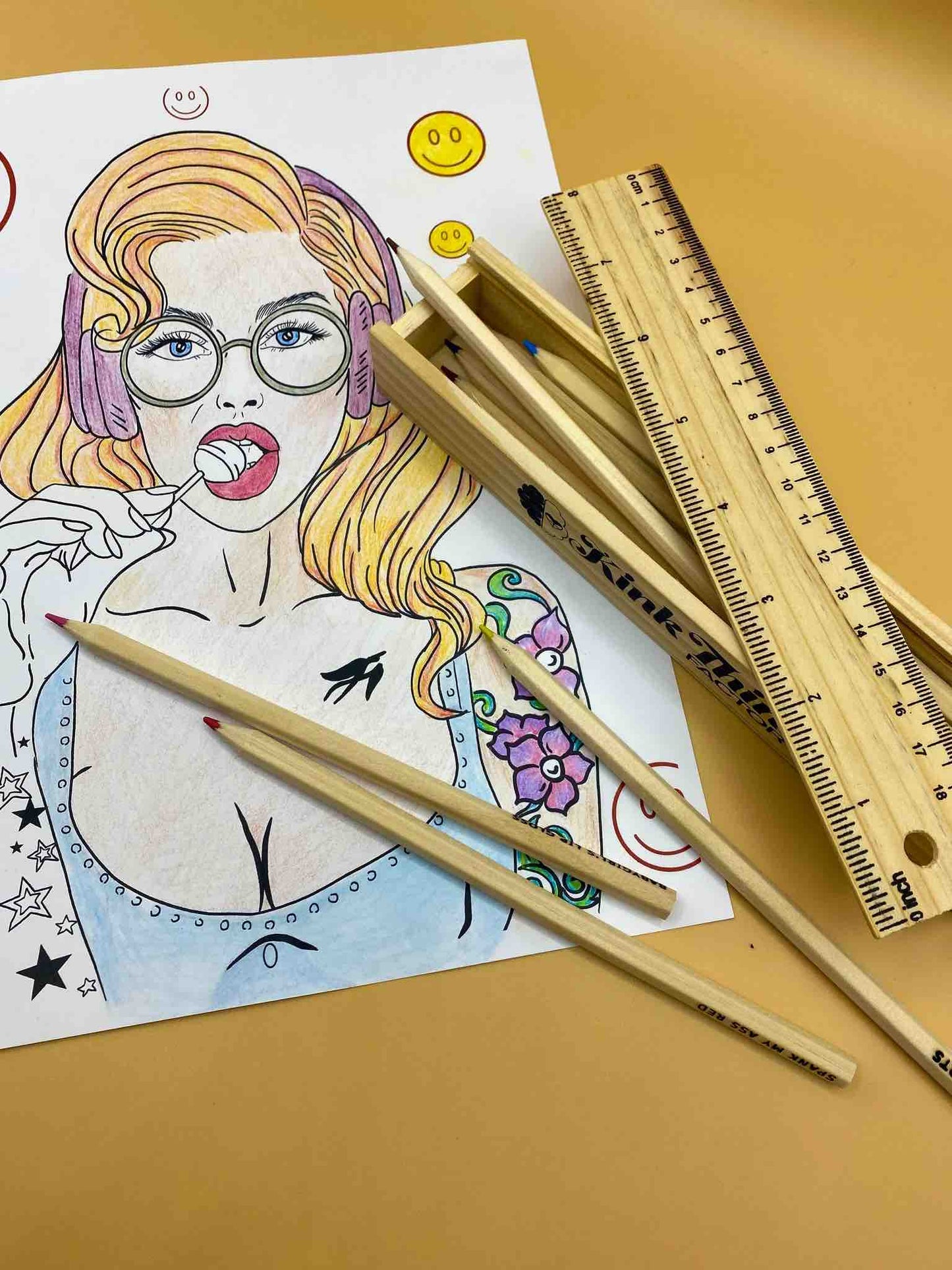A page from Naughty and Nice: A Coloring Book for Babygirls: A half colored illustration of girl in a low cut top with a lollipop in her mouth.  Sitting atop the right side of the page is a box of colored pencils and a ruler.