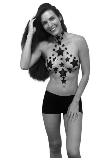 A model standing against a white background wearing black shorts and the Dom Squad Starry Stick On Pasties Crop Top in a decorative pattern on their chest and neck.