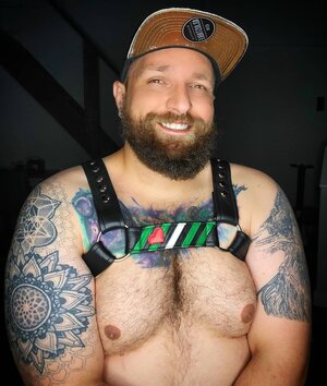A model showing the front of a harness with the Daddy/Boi Pride Flag Center Strap. 