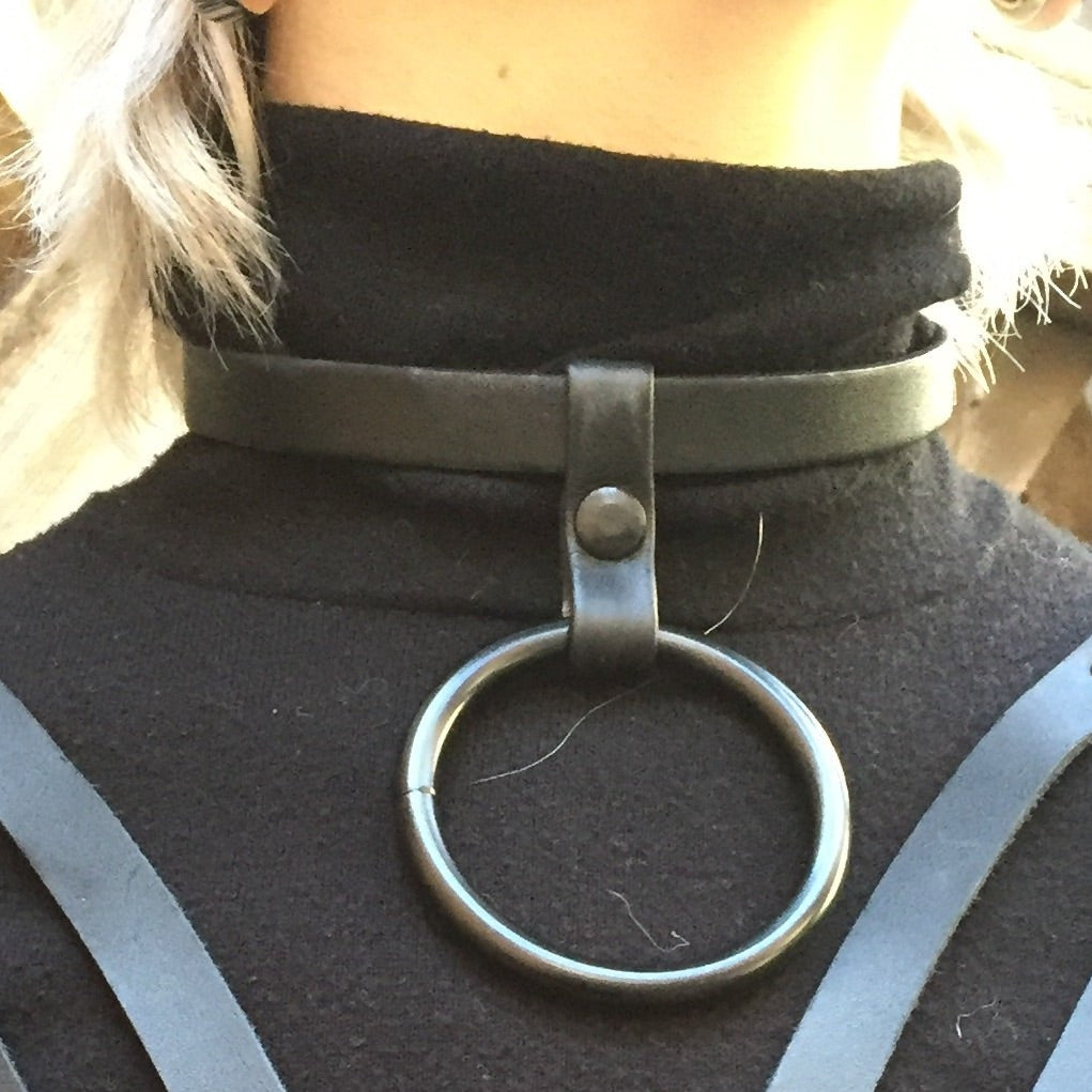 The black and silver Skinny Leather Collar with Large Drop Ring in silver on a model wearing a chest harness.