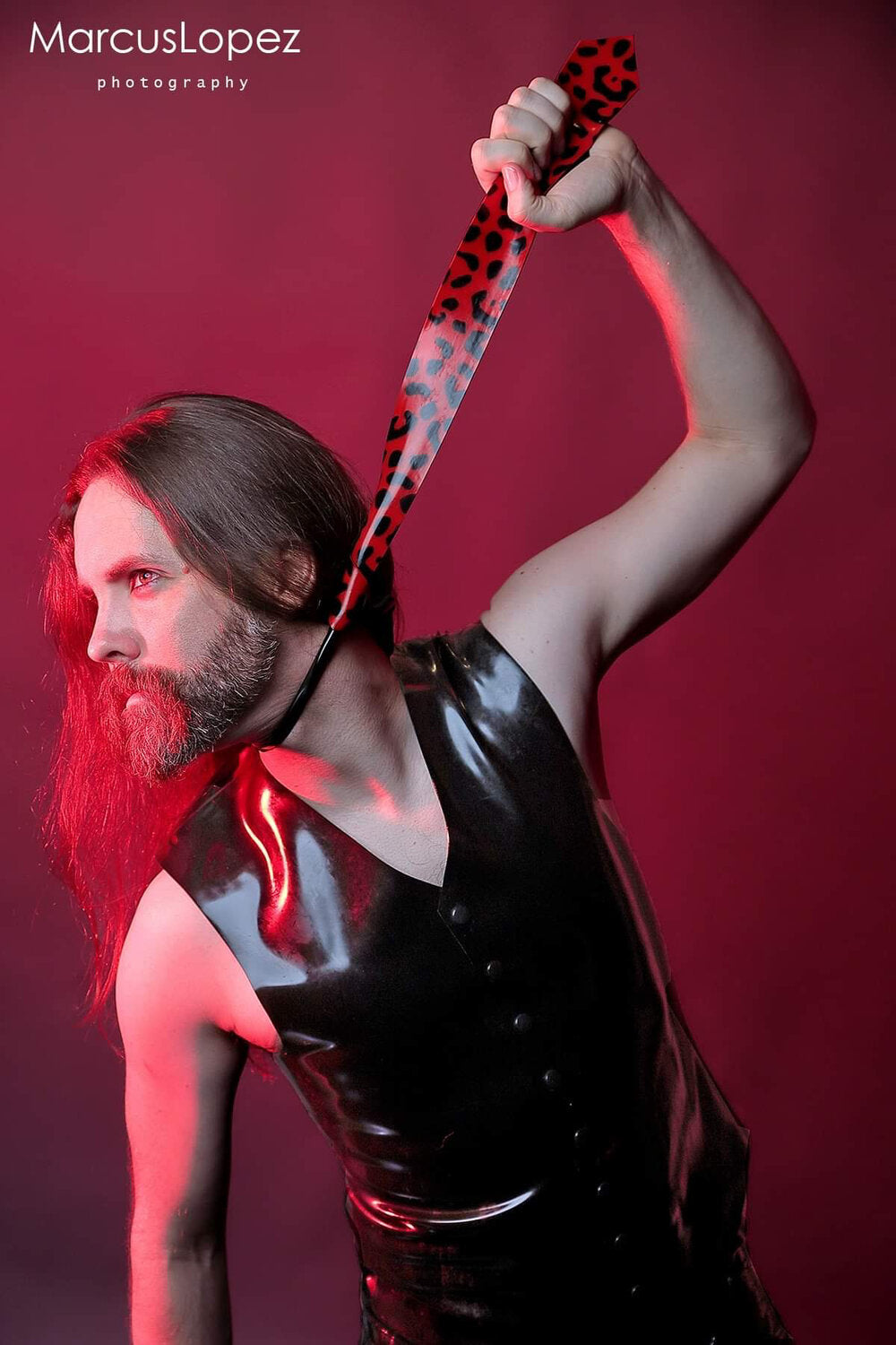 A model showing the front of the black Latex Snap Vest holds a red and black latex tie up like they are choking themselves.
